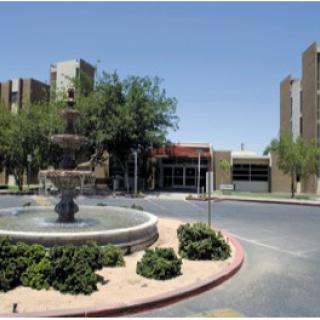 A scenic view of a fountain surrounded by buildings and trees on a sunny day.