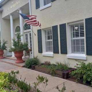 A building with white columns and an American flag, surrounded by potted plants and landscaping.