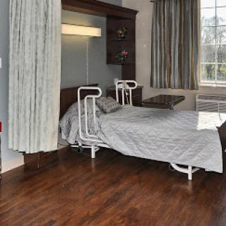 A well-furnished hospital room featuring a hospital bed, bedside table, and large windows providing natural light.