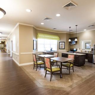 A modern dining area with a kitchen setup, featuring tables and chairs under bright lighting.