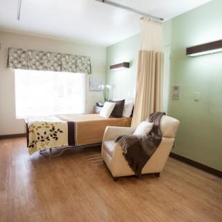 A bright and inviting hospital room featuring a bed, a comfortable chair, and natural light coming through the window.