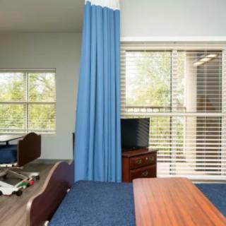 A hospital room featuring a patient bed, curtain divider, and a window with blinds.
