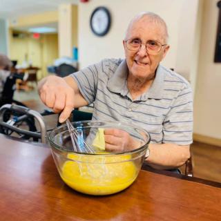 An elderly man happily mixing ingredients in a bowl.