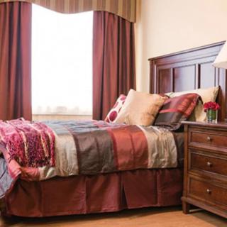 A cozy bedroom with warm-colored bedding, a wooden nightstand, and soft lighting.