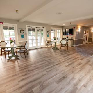 A spacious and well-lit dining area with wood flooring, featuring tables and chairs near large windows.