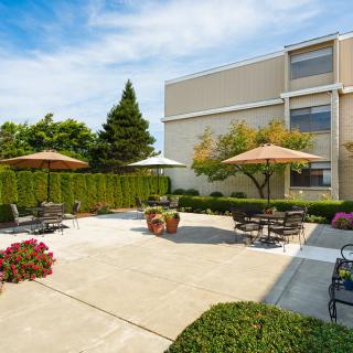 A well-maintained outdoor patio area with tables, chairs, and umbrellas, surrounded by greenery.