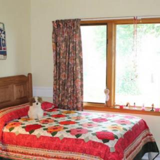 A cozy bedroom with a colorful quilt and a cat sitting on the bed.