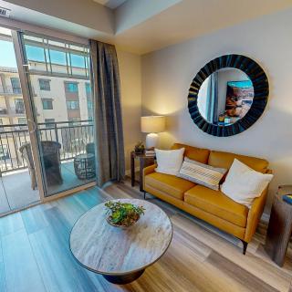 A modern living room with a mustard sofa, circular mirror, and access to a balcony.