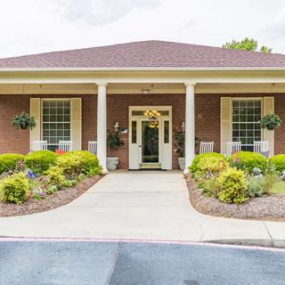 A well-maintained building entrance with a brick exterior and landscaped front yard.