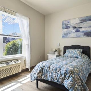 A cozy bedroom with a single bed, illuminated by natural light from a large window.