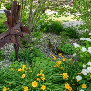 A serene garden scene with flowers, a duck, and a metal sculpture.