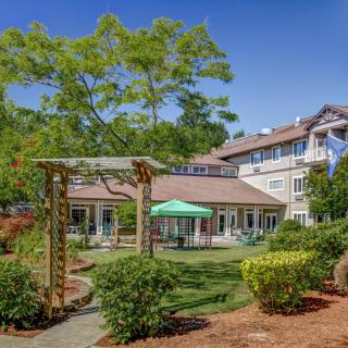 A beautifully landscaped garden with a gazebo, surrounded by trees and shrubs in front of a house.