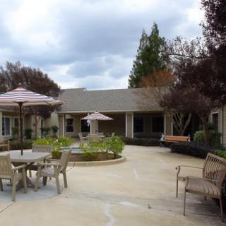 A peaceful outdoor patio area with tables, chairs, and umbrellas surrounded by landscaped gardens.