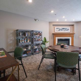 A cozy living room with a fireplace, surrounded by bookshelves and a neatly arranged table and chairs.