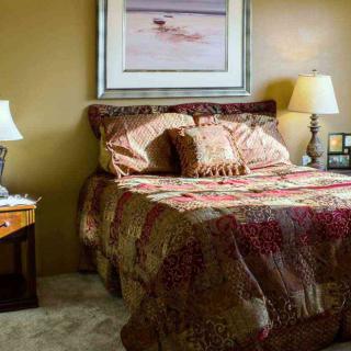 A cozy bedroom with a neatly made bed, two lamps on nightstands, and a painting above the headboard.