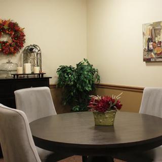 A cozy dining room with a round table surrounded by upholstered chairs, decorated with a centerpiece and seasonal wreath.