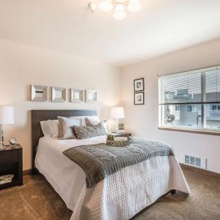 A modern and minimalist bedroom featuring a neatly made bed with gray and white bedding, bedside tables with lamps, and wall decorations.