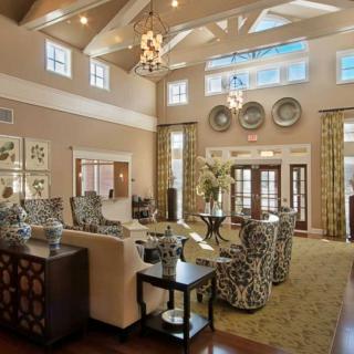 A spacious and elegantly designed living room with luxurious furniture and chandeliers, featuring a high ceiling and large windows.