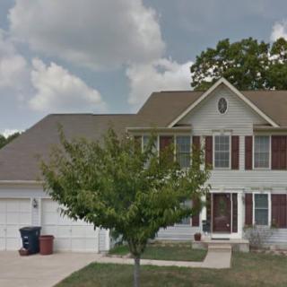 A suburban house with a front yard tree and driveway under a cloudy sky.