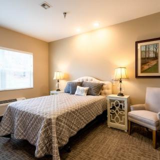 A cozy bedroom with a neatly made bed, two lamps, and a comfortable chair beside a window.
