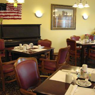 A cozy restaurant dining area with neatly set tables, a piano, and an American flag on the wall.
