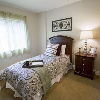 A cozy bedroom with a single bed and decorative pillows beside a nightstand and lamp.