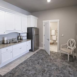 A modern kitchen area with white cabinets and a stainless steel refrigerator, featuring an adjacent open door leading to another room.