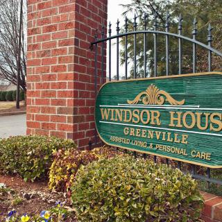 Entrance sign for Windsor House located in Greenville, featuring a brick structure and greenery.