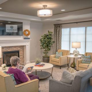 A cozy living room with a person reading near a fireplace, surrounded by comfortable seating and decor.