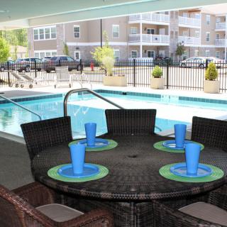 An outdoor dining area with a table set near a swimming pool, surrounded by apartment buildings.