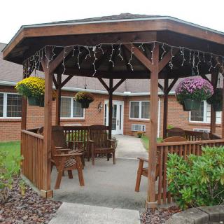 A wooden gazebo with hanging plants and benches in a garden setting.
