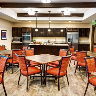 A modern dining and kitchen area with wooden tables, orange chairs, and stylish lighting.
