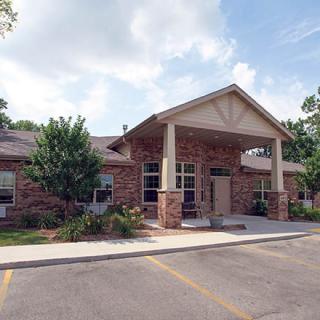 A brick building with an entrance and surrounding greenery under a partly cloudy sky.