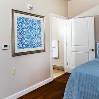 A bedroom featuring a blue-themed decor, with a framed artwork on the wall and an open doorway leading to another room.