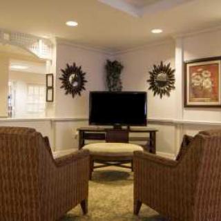 A cozy living room setup with wicker armchairs facing a television, complemented by decorative artwork and plants.