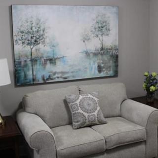A cozy living room with a gray sofa, decorative cushion, and a serene landscape painting on the wall.