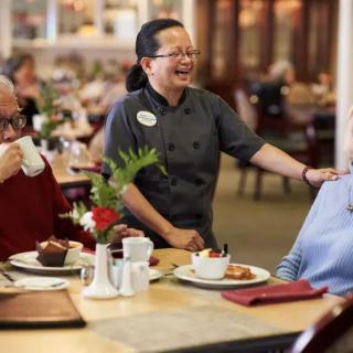 A waitress shares a laugh with an elderly couple during their dining experience at a restaurant.