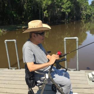 A person wearing a hat is fishing from a dock by the lake.