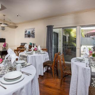 A well-decorated dining area with round tables set for a meal, featuring elegant tableware and white linens, facing a sliding glass door leading outside.