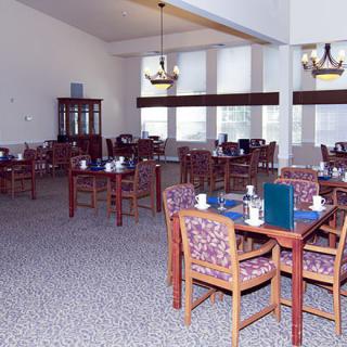 An empty dining room with multiple tables and chairs, decorated with chandeliers and a carpeted floor.