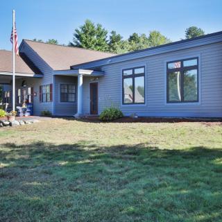 A modern single-story house with a lawn and flagpole, set against a backdrop of trees on a clear day.