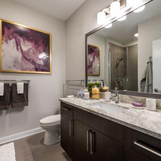 A modern bathroom featuring a large mirror, dark vanity with marble countertop, and abstract artwork.