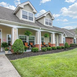 A well-maintained house with a spacious porch and lush green lawn under a blue sky.
