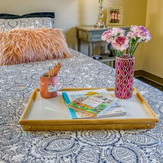A cozy bedroom setup with a stylish tray on the bed, featuring flowers in a vase, books, and a soft pillow.