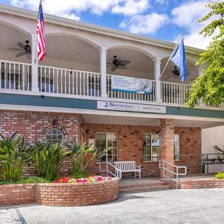 A two-story building entrance with a balcony, decorated with flags and surrounded by plants.