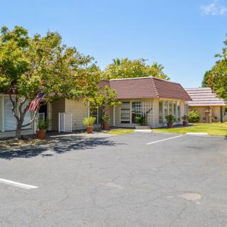 A small motel with a parking lot surrounded by trees under a clear blue sky.