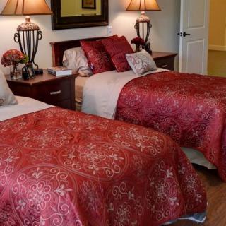 A cozy bedroom with two twin beds adorned with red covers and elegant lighting.