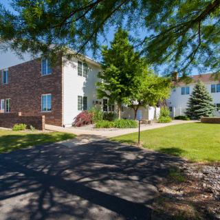A sunny day view of a residential apartment building surrounded by trees and a grassy area.