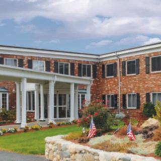 A brick building with white pillars and landscaping featuring small flags.