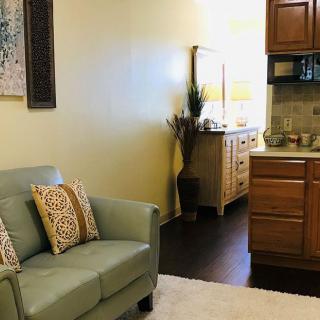 A cozy living room with a green sofa and a view of the kitchen area featuring wooden cabinets.